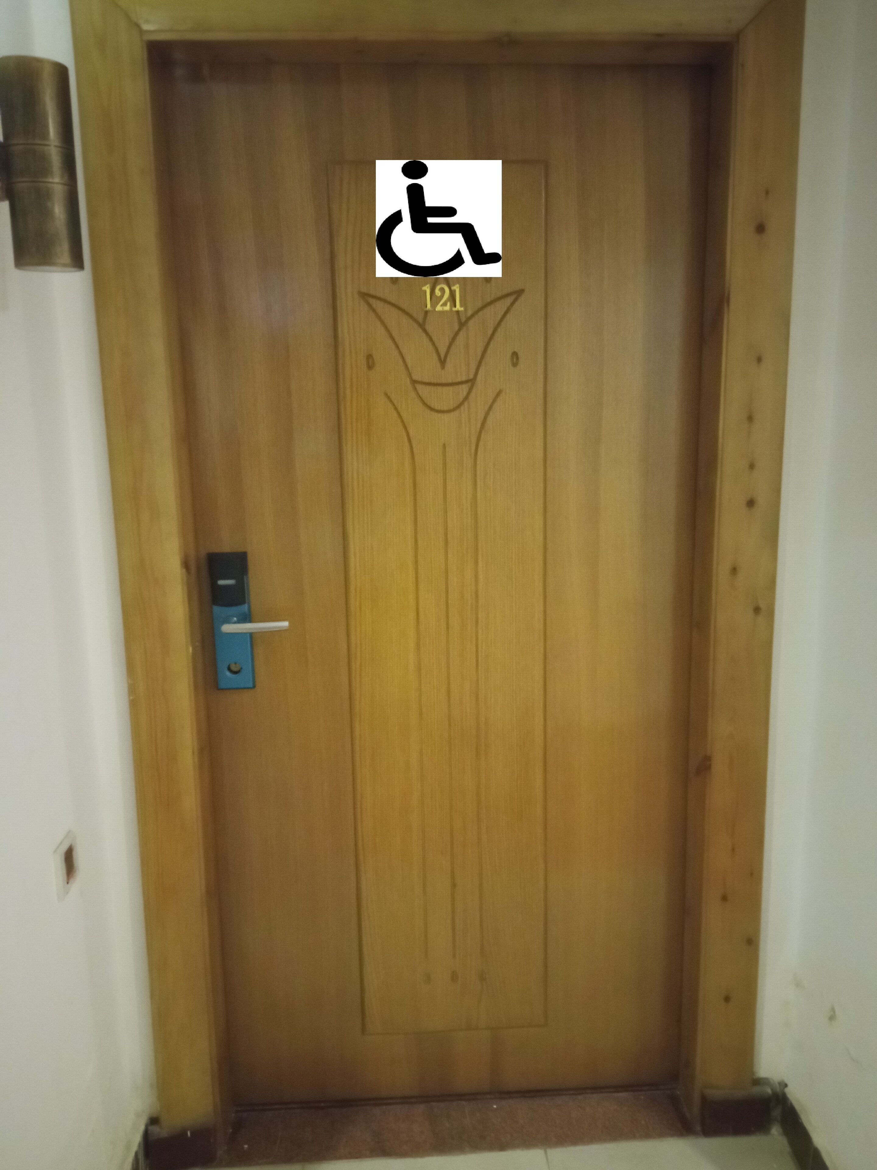 Une porte en bois portant le symbole d’accessibilité pour les personnes en fauteuil roulant et le numéro 121.