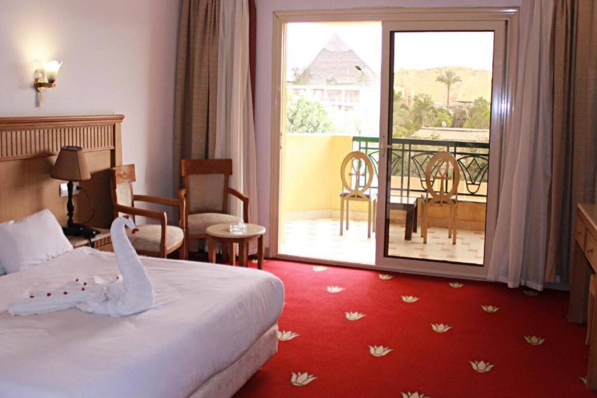 A hotel room with a bed, a chair, a small table, and a balcony with chairs.