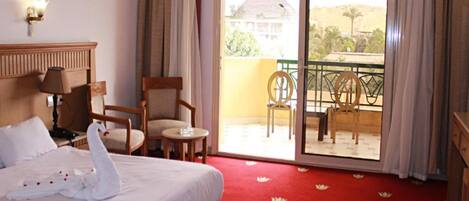 Una habitación de hotel con una cama, una silla, una mesita y un balcón con sillas.