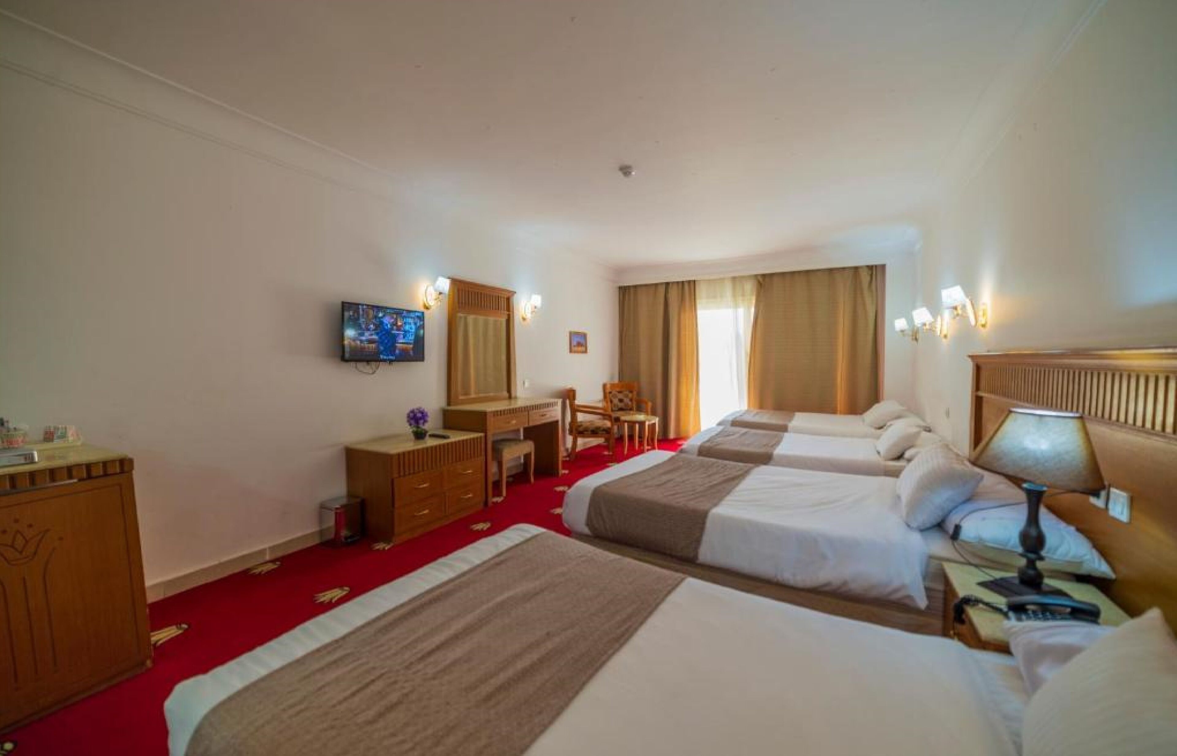 A hotel room with two beds, a desk, a chair, a television, and a lamp.