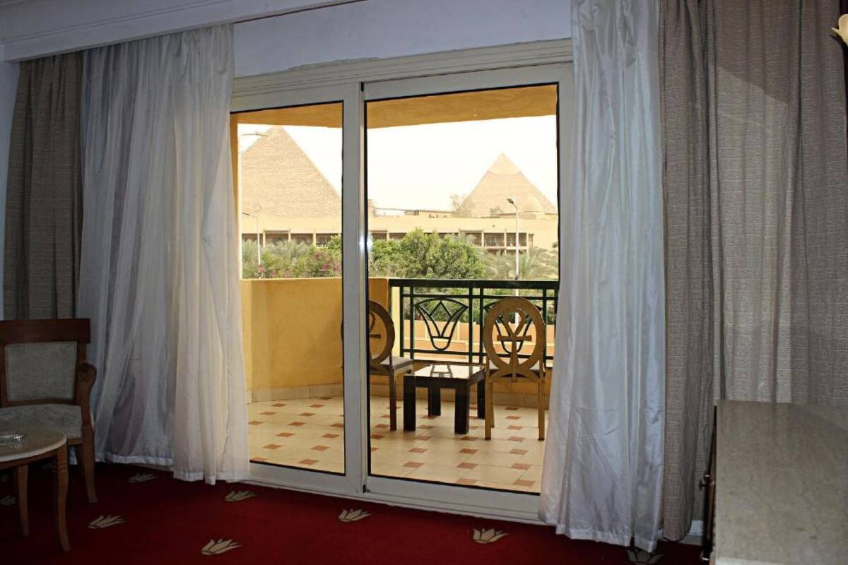 A room with a sliding glass door leading to a balcony with a view of pyramids.