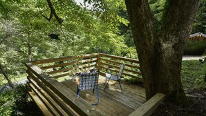 A wooden deck with two chairs and a bench, surrounded by trees. - The Tulip Poplar Cabin - Perfect for Two People (Topton)