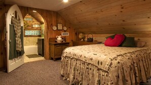 A cozy bedroom with a wooden ceiling, a bed with floral bedding, a heart-shaped pillow, and a small table with a pitcher and bowl. - The Tulip Poplar Cabin - Perfect for Two People (Topton)
