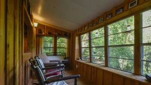 A cabin interior with a wooden bench, a table, and large windows offering a view of the forest. - The Tulip Poplar Cabin - Perfect for Two People (Topton)