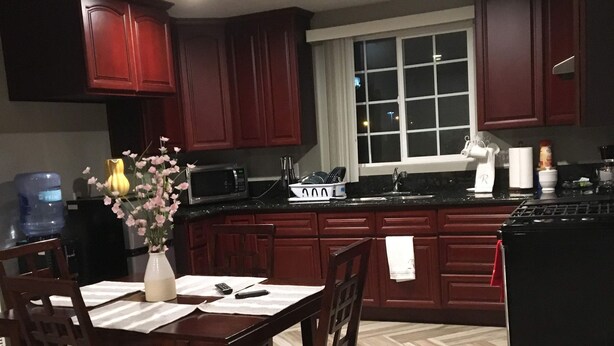 A modern kitchen with dark wooden cabinets, a central island, and a dining area with a table and chairs. - Rigo’s Apartment  (South Gate)