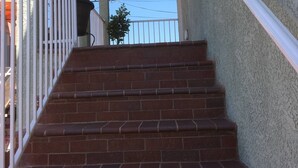 A staircase with a white railing leading to a covered area with a textured wall and a ceiling light. - Rigo’s Apartment  (South Gate)