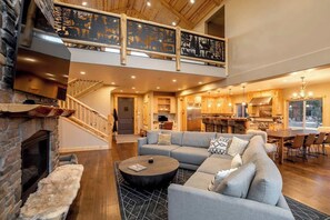A spacious living area with a fireplace, a large sofa, a dining table, and a kitchen in the background.