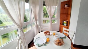 A dining area with a round table set for breakfast, including croissants and orange juice, with a view of greenery outside. - Apartamento Lurra Barrika (Barrika)