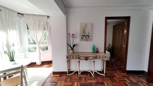 A room with a wooden herringbone floor, a white table with chairs, a console table with decorative items, and a painting on the wall. - Apartamento Lurra Barrika (Barrika)