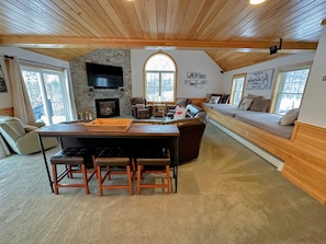 Un salon chaleureux avec une cheminée en pierre, un plafond en bois et une grande fenêtre.