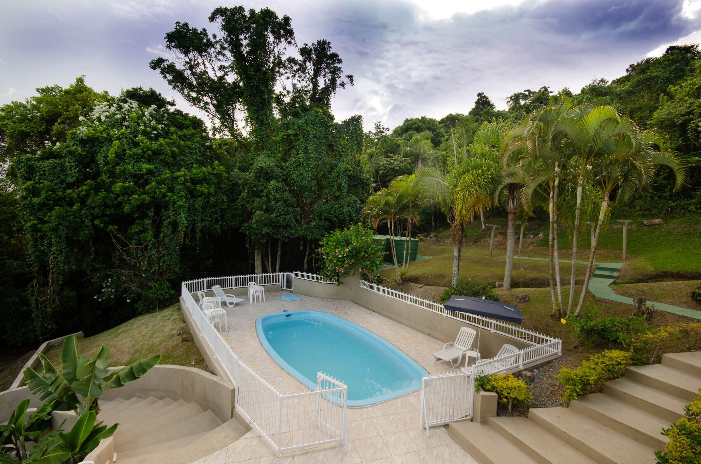 A swimming pool with a white fence, surrounded by lush greenery and palm trees.