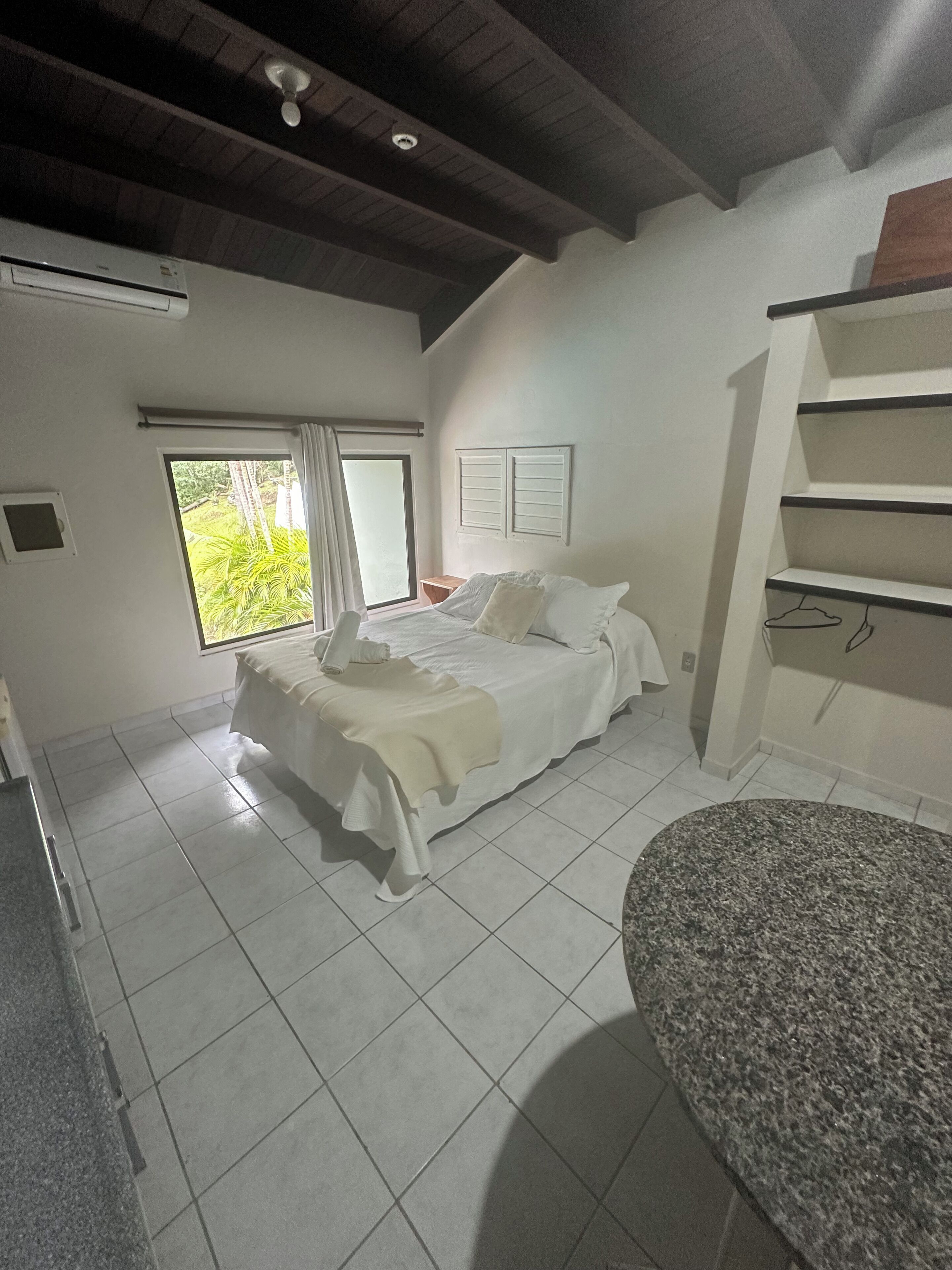 Quarto com cama, janela, ventilador de teto e prateleira embutida.