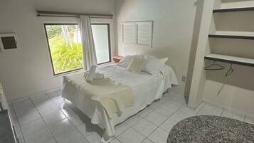 Quarto com cama, janela, ventilador de teto e prateleira embutida.