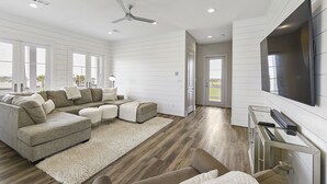 A spacious living room with a sectional sofa, a flat-screen TV, and a ceiling fan.