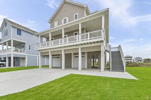 A two-story residential building with a covered front porch, multiple garage doors, and a staircase leading to an upper level. - Relax and enjoy at Alamo Sea! Two king suites! (Galveston)