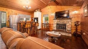 A cozy cabin interior with a wooden ceiling, a stone fireplace, a bar area, and a comfortable seating area.