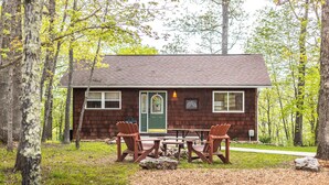 A cabin with a green door, a window, and a sign that reads "Cottage." There is a table with chairs in front of the cabin.