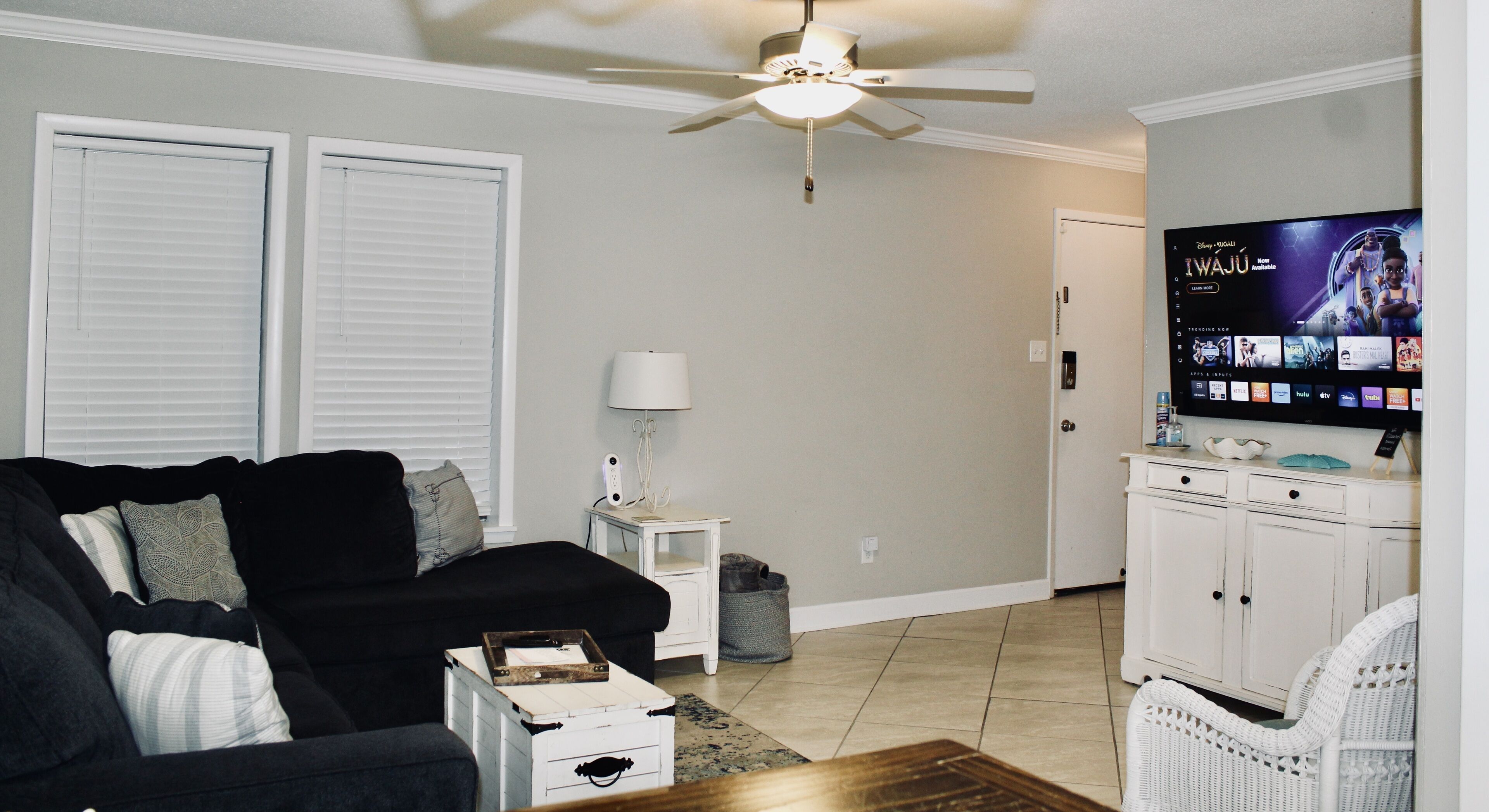 A living room with a black sofa, a white side table, a lamp, a television, and a white cabinet.