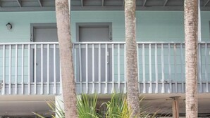 A building with a light green facade, white balconies, and palm trees in the foreground.