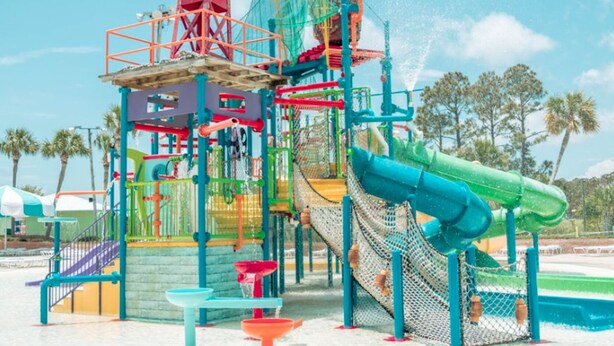 A water play area with slides, climbing structures, and a netted climbing wall.