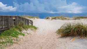 A sandy beach with a wooden fence on the left and a grassy dune on the right.