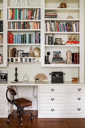 A study room with a wooden desk, a leather chair, and a bookshelf filled with books and decorative items.