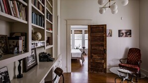 A room with a wooden floor, a red armchair, a white bookshelf, and a door leading to another room. - Elegant Historic Estate: Professionally Designed (Austin)