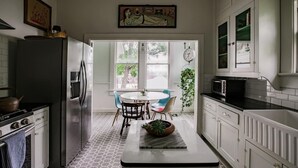 A kitchen with white cabinets, a refrigerator, a stove, and a dining area with a table and chairs. - Elegant Historic Estate: Professionally Designed (Austin)