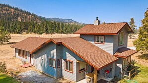 A two-story house with a red-tiled roof, a large window, and a patio with outdoor furniture. - Mountain Breeze - Pet Friendly Read Our Reviews (Weed)