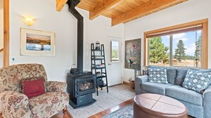 A cozy living room with a fireplace, a sofa, a chair, and a large window with a view of trees. - Mountain Breeze - Pet Friendly Read Our Reviews (Weed)