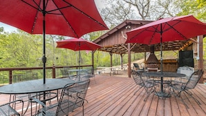 A wooden deck with outdoor seating, including tables and chairs, and red umbrellas providing shade. - Spacious hunting lodge hideaway with stunning views and Private River Access (Steelville)
