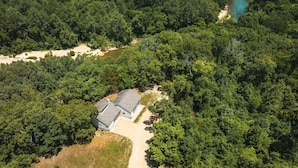 An aerial view of a house surrounded by dense forest, with a visible dirt path leading to the entrance. - Spacious hunting lodge hideaway with stunning views and Private River Access (Steelville)