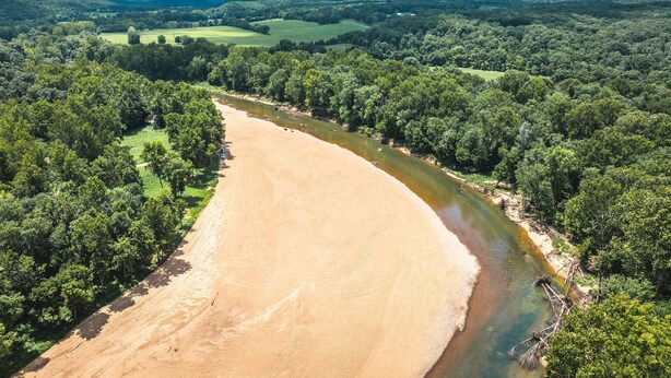 A river winding through a forested landscape with a sandy beach area. - Spacious hunting lodge hideaway with stunning views and Private River Access (Steelville)