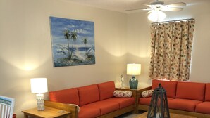 A living room with a sofa, two side tables, a coffee table, a chair, a rug, a painting, and a ceiling fan.