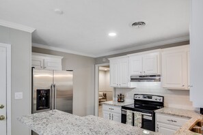 A modern kitchen with white cabinetry, stainless steel appliances, and a granite countertop. - Cheerful, Relaxing Home Away From Home! (Jackson)