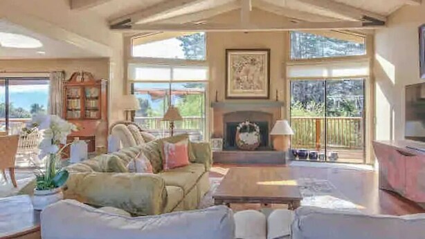 A spacious living room with a high ceiling, a fireplace, and large windows offering a view of the outdoors. - Beautiful Carmel House
 (Carmel)
