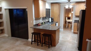 A modern kitchen with a central island, bar stools, a refrigerator, and a television.