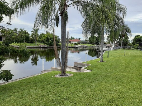 Ein gepflegter Rasen mit einem kleinen Teich, umgeben von Palmen und einem Gebäude im Hintergrund.