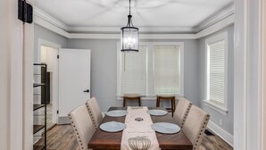 A dining room with a wooden table, beige upholstered chairs, a chandelier, and a decorative runner. - Royal Chateau in the heart of Fondren! (Jackson)