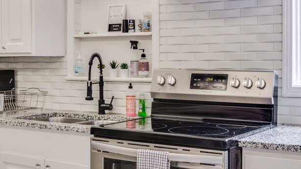A modern kitchen with white cabinetry, a stainless steel stove, and a backsplash with a brick pattern. - Royal Chateau in the heart of Fondren! (Jackson)