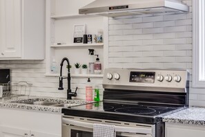 Una cucina moderna con mobili bianchi, piano cottura in acciaio inossidabile e schienale con motivo a mattoni.