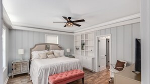 A bedroom with a bed, a pink bench, a ceiling fan, a TV, and a white wardrobe. - Royal Chateau in the heart of Fondren! (Jackson)