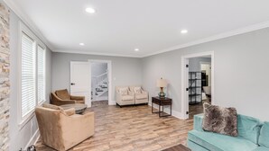 A spacious living room with a wooden floor, a beige sofa, a teal sofa, and a small table with a lamp. - Royal Chateau in the heart of Fondren! (Jackson)