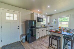 A modern kitchen with white cabinets, a black refrigerator, a microwave, and a sink. There is a window with a view of greenery outside.