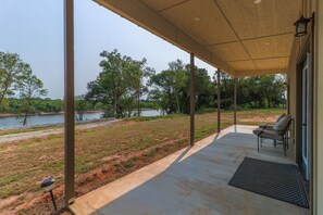 A covered outdoor area with a view of a lake and trees. There are two chairs and a small table.