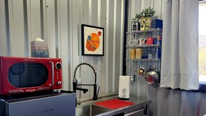 Una cocina compacta con un microondas rojo, un lavamanos de acero inoxidable y una pequeña encimera.