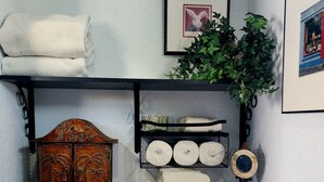 Un baño con un inodoro blanco, un estante con toallas, un cuadro enmarco y una planta en maceta.