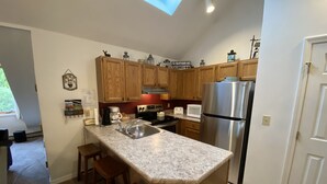 A kitchen with wooden cabinets, a stainless steel refrigerator, a granite countertop, and a built-in oven. - PicoVillage Resort G301-Beautiful contemporary style 2-bedroom,2-bath condo with the comfort of home (Killington)