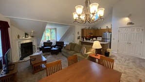 A spacious living room with a fireplace, a dining area, a kitchen, and a loft bedroom with a large window. - PicoVillage Resort G301-Beautiful contemporary style 2-bedroom,2-bath condo with the comfort of home (Killington)