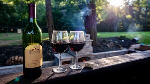 Une bouteille de vin et deux verres sur une surface en bois, avec un jardin en arrière-plan.